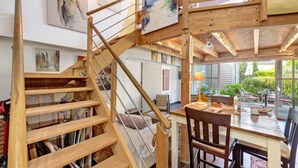 A wooden staircase leading to a dining area with a table and chairs, and artwork on the walls.