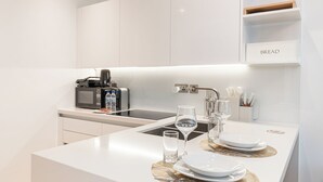 Una cocina moderna con microondas integrado, tostadora y lavabo. Hay dos platos, dos vasos y un juego de cuchillos sobre la encimera.