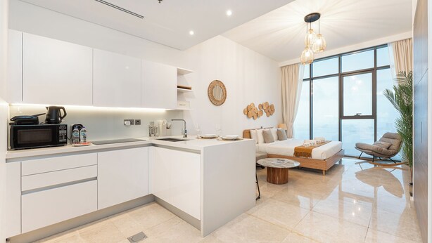 Una cocina moderna con armarios blancos, una isla central y un comedor con sofá y sillón.