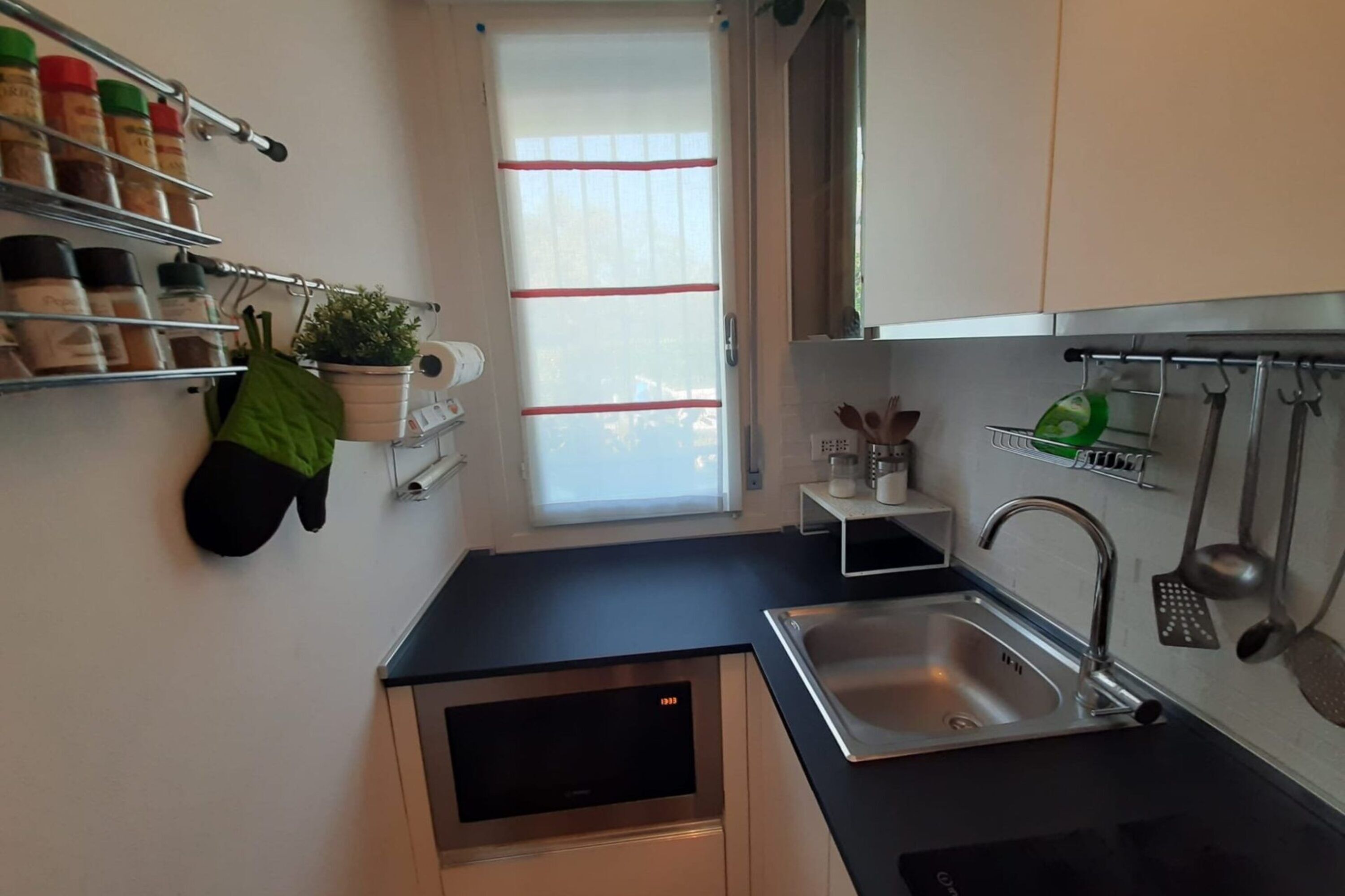 A compact kitchen with a built-in dishwasher, a sink with a faucet, and a window with blinds.