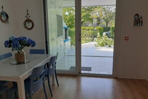 Ein Zimmer mit Glastür zu einem Außenbereich, einem Esstisch mit Stühlen und einem Blumentopf.