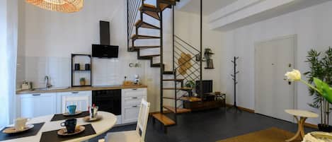 A modern kitchen with white cabinets, a black TV, and a wooden staircase.