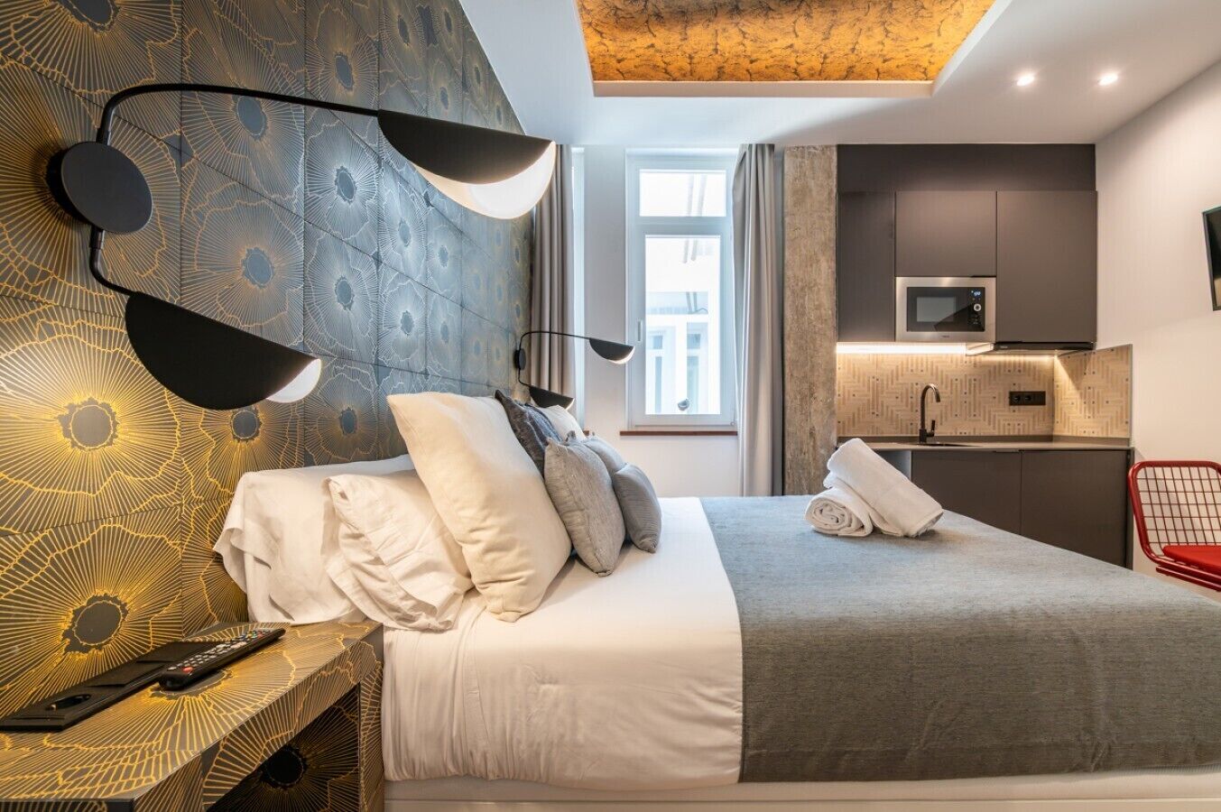 A modern hotel room with a bed, bedside table, lamp, and a view of the city.