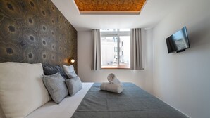 Une chambre d’hôtel avec un lit, un téléviseur à écran plat, une fenêtre avec des rideaux et un mur décoré d’un motif.