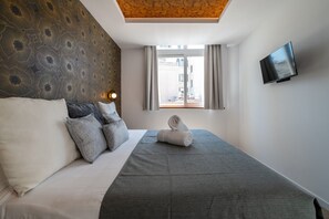 A hotel room with a bed, a flat-screen TV, a window with curtains, and a patterned wall. - 505 - A33 Signature | Penthouse | Terr | 2BR | 6G (Madrid)