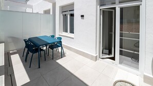 Une terrasse avec une table et des chaises, une porte-fenêtre coulissante et un mur extérieur blanc.