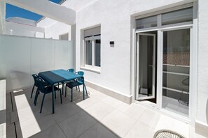 A patio with a table and chairs, a sliding glass door, and a white exterior wall. - 505 - A33 Signature | Penthouse | Terr | 2BR | 6G (Madrid)