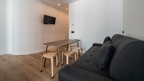 Ett modernt vardagsrum med en mörk soffa, ett matbord i trä med stolar och en platt-TV som är monterad på väggen.
