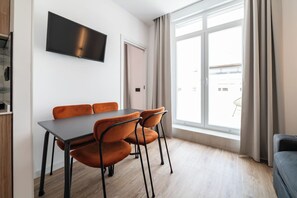 Et moderne værelse med spisebord, stole, et fladskærms-tv og et stort vindue med gardiner.