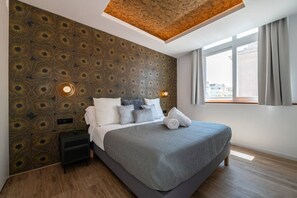 A modern bedroom with a patterned wall, a large bed with grey bedding, a nightstand, and a window with curtains. - A33 Signature | Penthouse | Terrace | 2BR | 6G (Madrid)