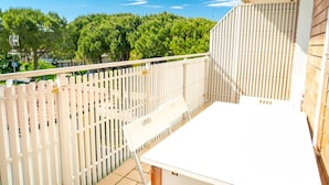 Un balcon avec une table et une chaise blanches, une clôture blanche et une vue sur les arbres et les bâtiments.