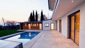 Une maison moderne dotée d’une piscine, d’un patio couvert et d’une grande porte vitrée.