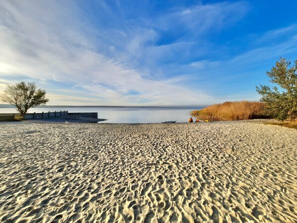 A sandy beach with a calm body of water, a wooden fence, and some vegetation.
