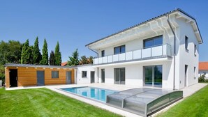 Une maison moderne à deux étages avec une piscine, une structure en bois attenante et une pelouse bien entretenue.