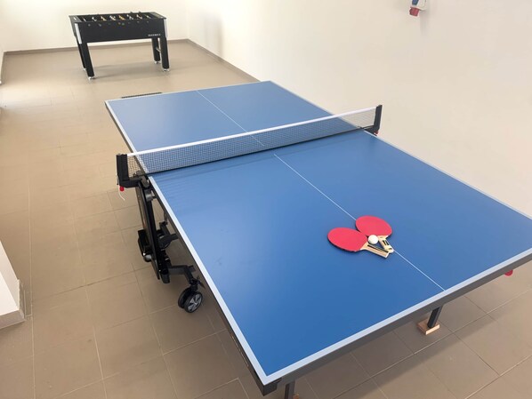 Une table de ping-pong bleue, avec un filet, deux raquettes rouges et une balle.