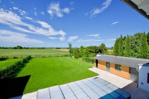 A modern house with a solar panel roof, a swimming pool, and a large green lawn.