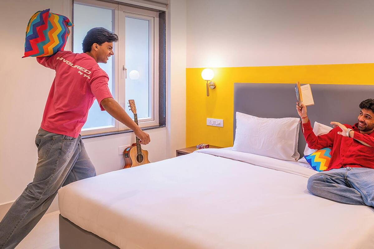 Quarto de hotel com uma cama, uma janela e uma mesa de cabeceira com abajur.