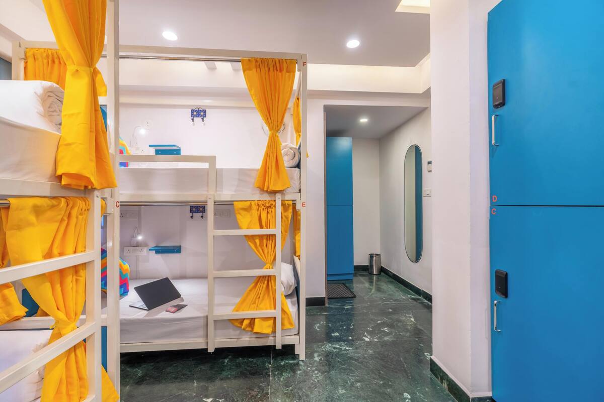 Um dormitório com cortinas amarelas, um laptop na cama de baixo e uma porta azul.