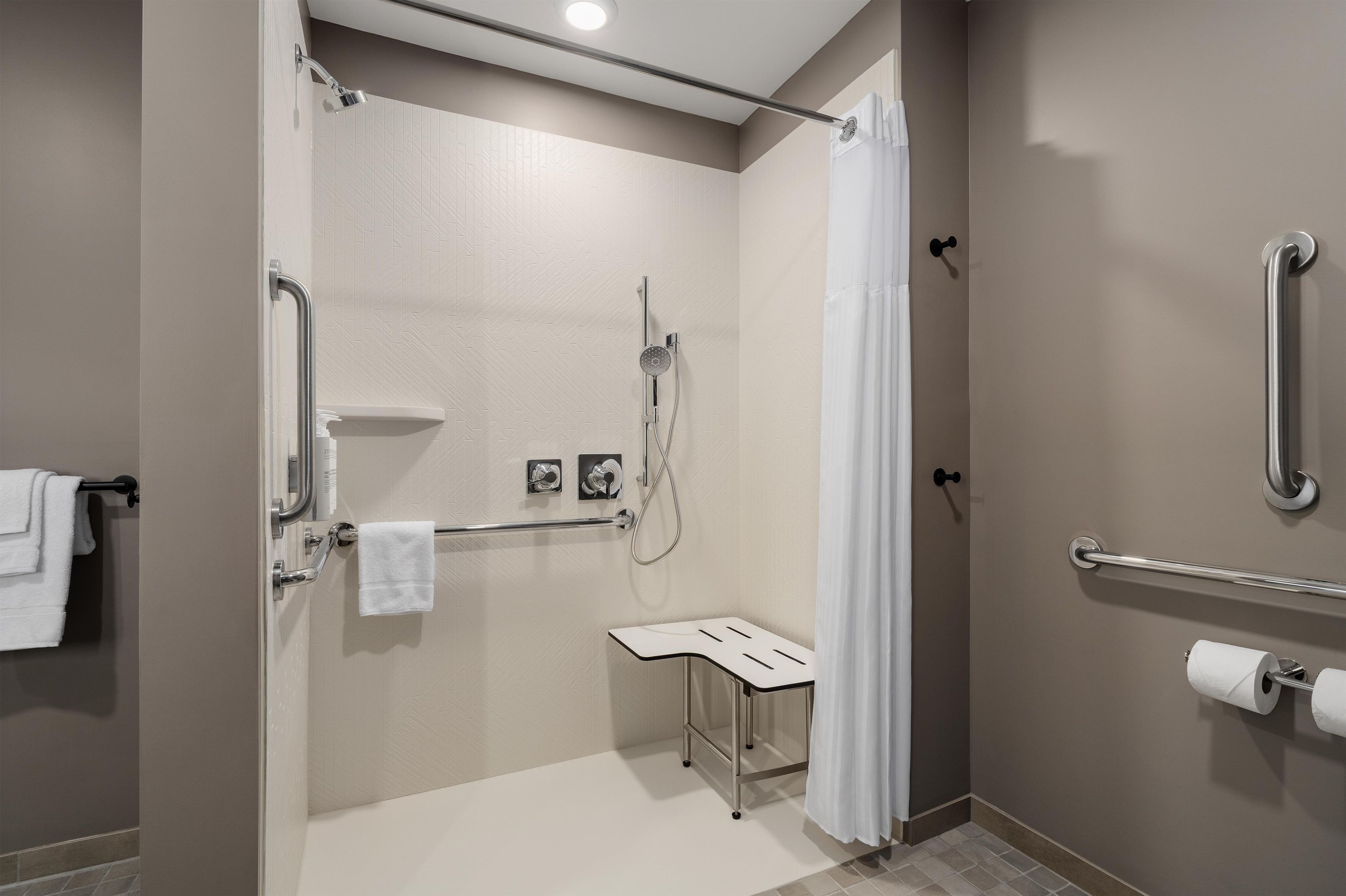 Un baño moderno con ducha a ras de suelo, barras de apoyo, un soporte para papel higiénico y un perchero para toallas.
