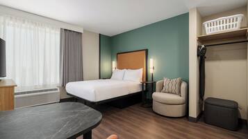 A hotel room with a bed, bedside tables, a desk, a chair, a TV, a heater, and a laundry basket.