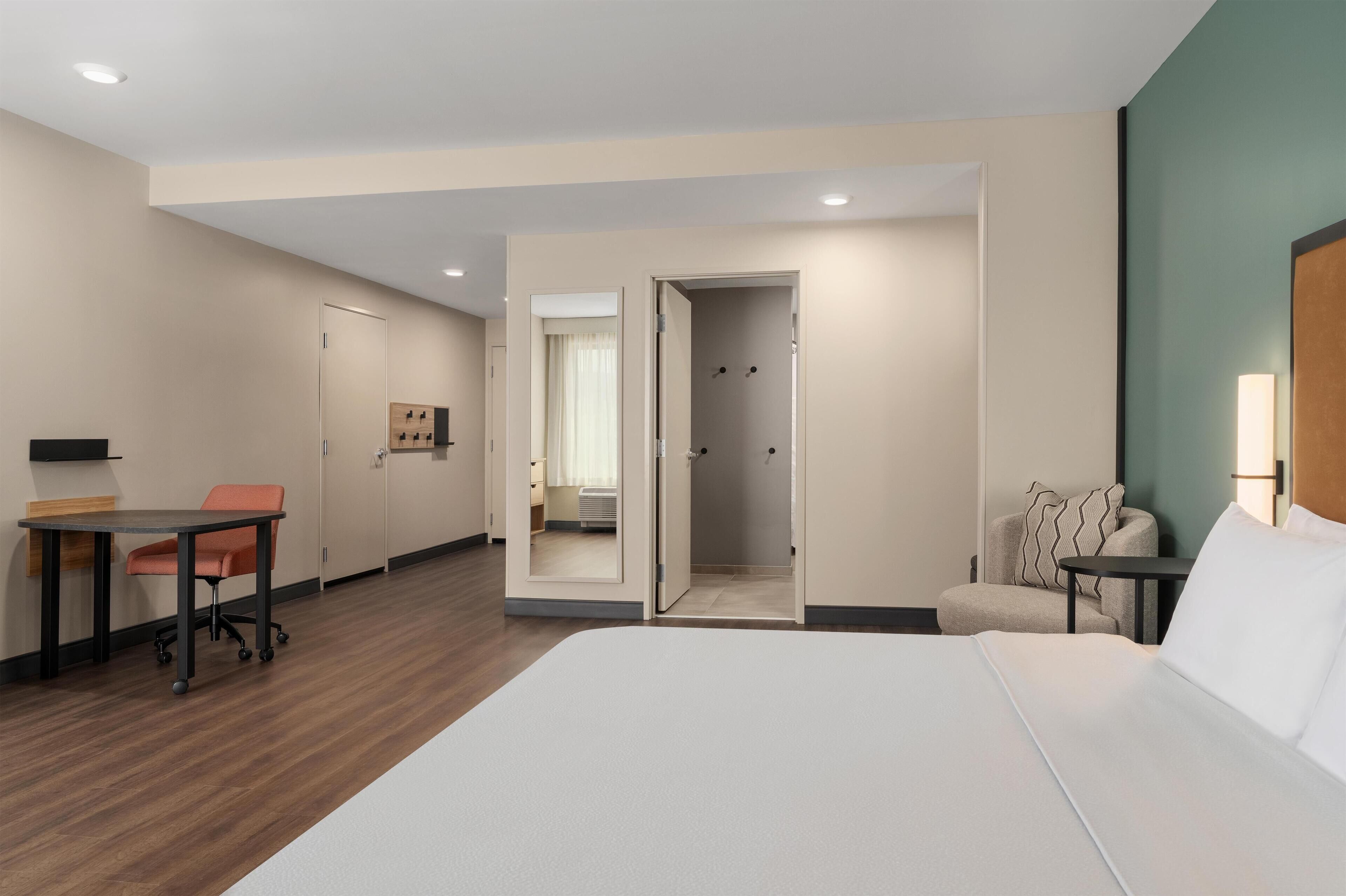 A hotel room with a bed, a desk, a chair, a sofa, and a mirror.