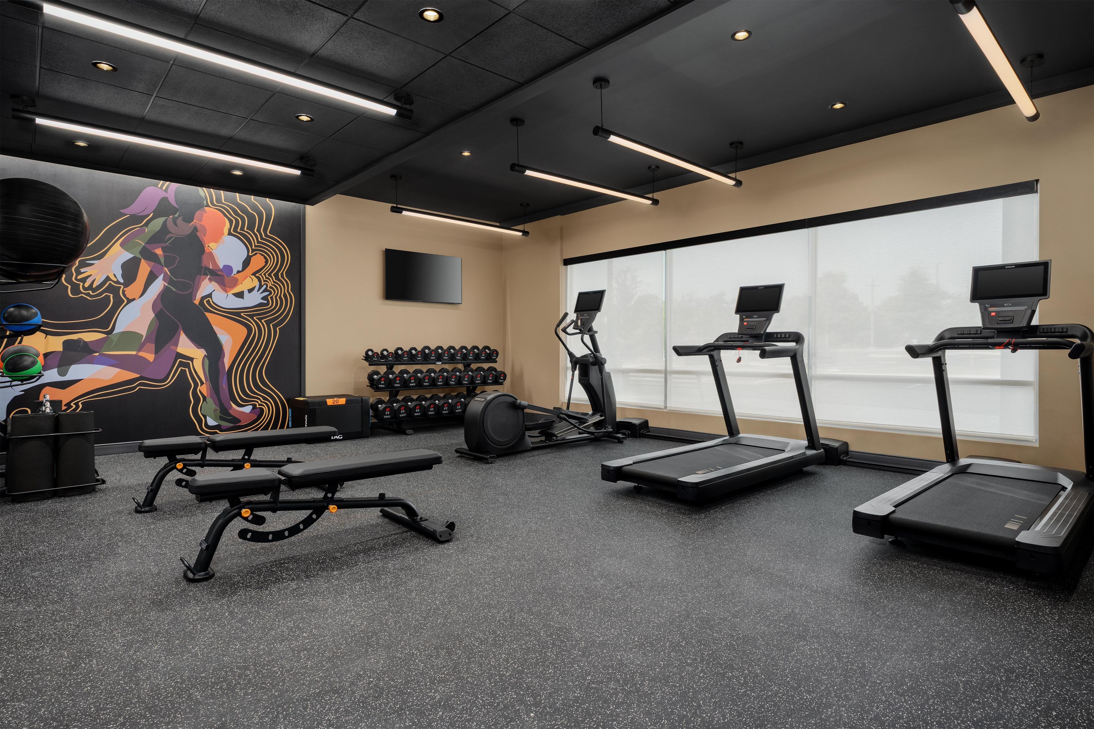 A gym with treadmills, weight benches, dumbbells, and a large motivational mural.