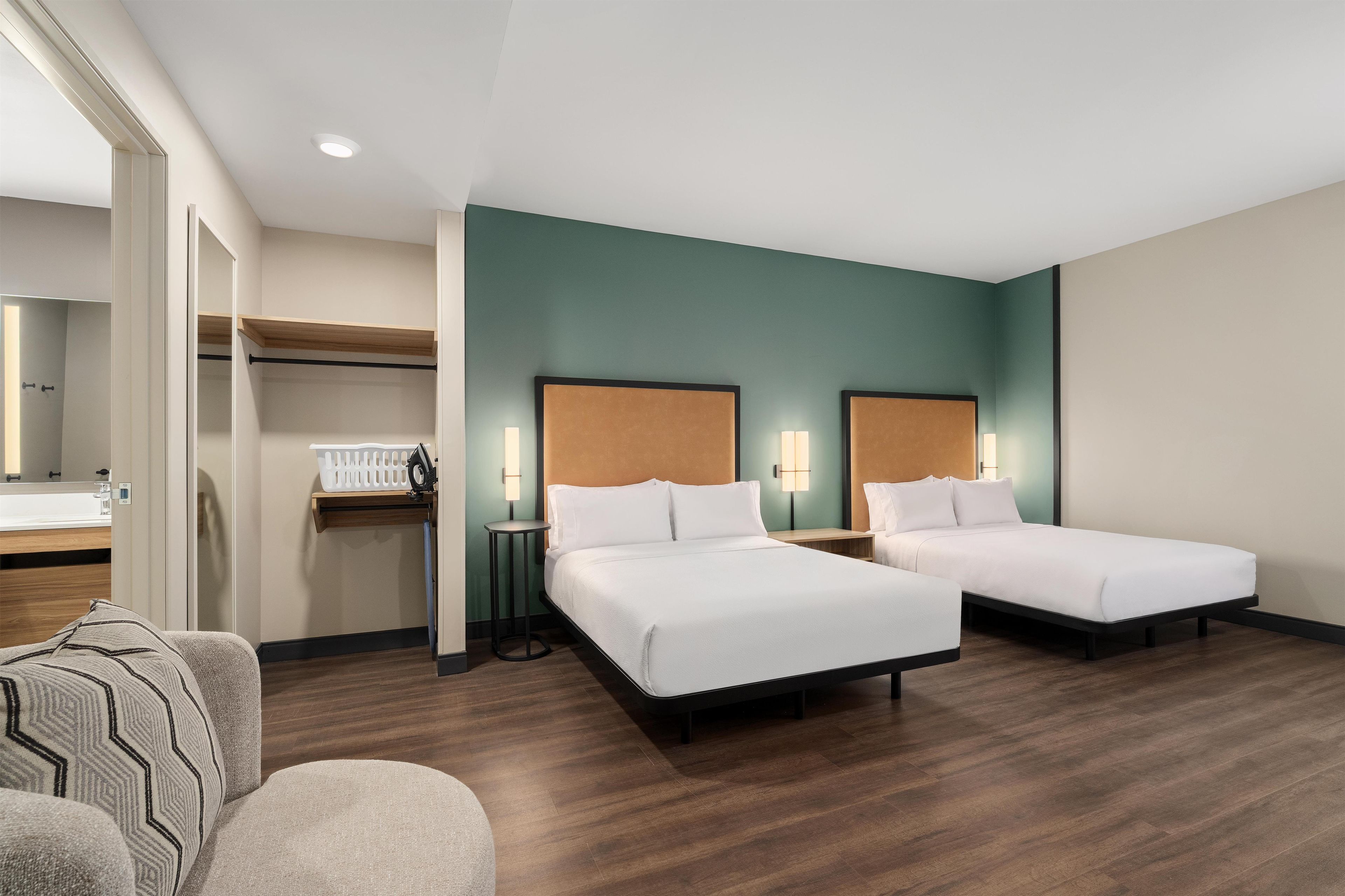 Quarto de hotel com duas camas, uma escrivaninha, uma cadeira e banheiro.