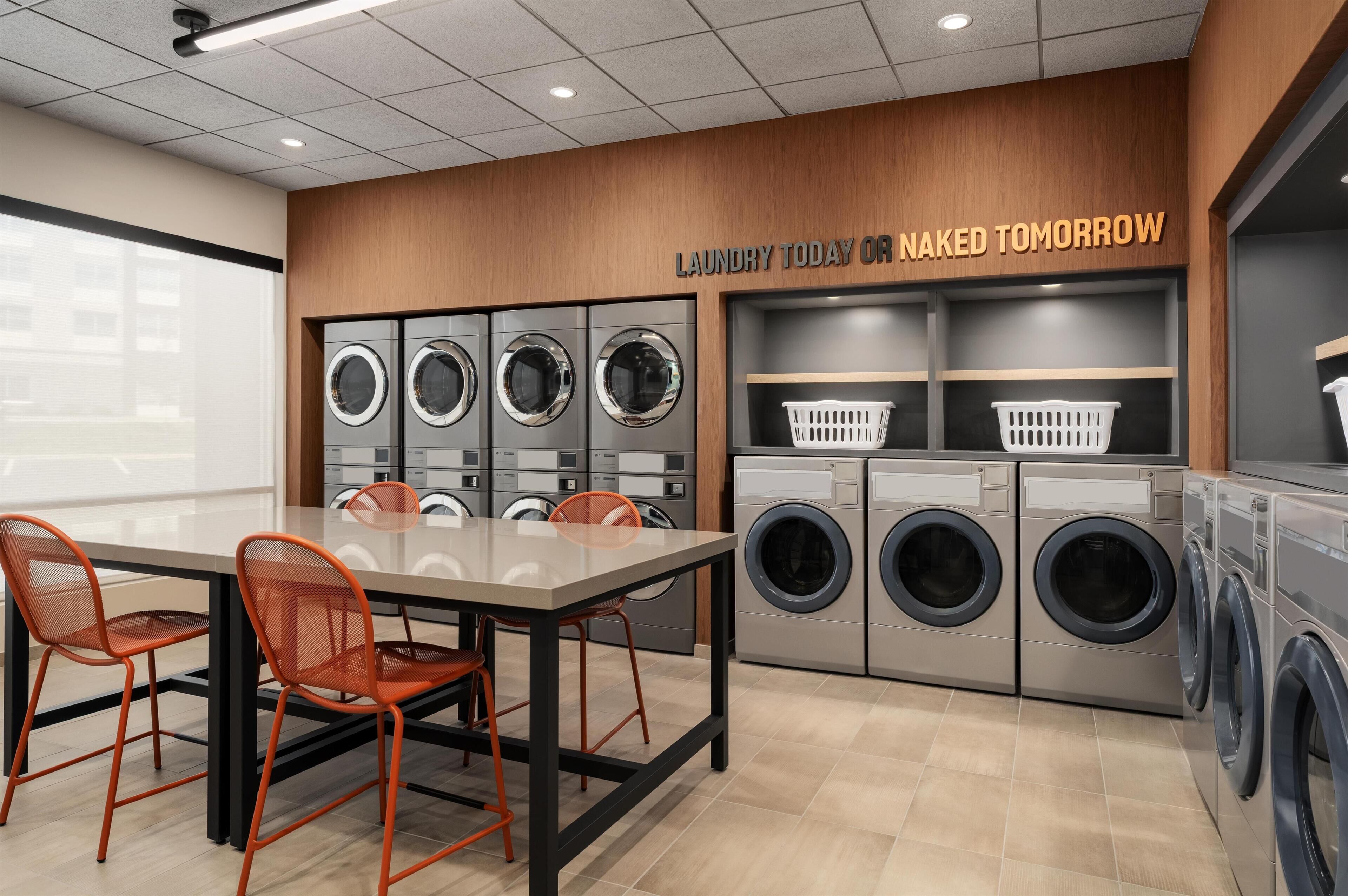 A modern laundry facility with multiple washing machines, a table with chairs, and a sign above.