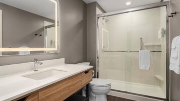 A modern bathroom with a glass-enclosed shower, a white sink, and a vanity with a mirror.