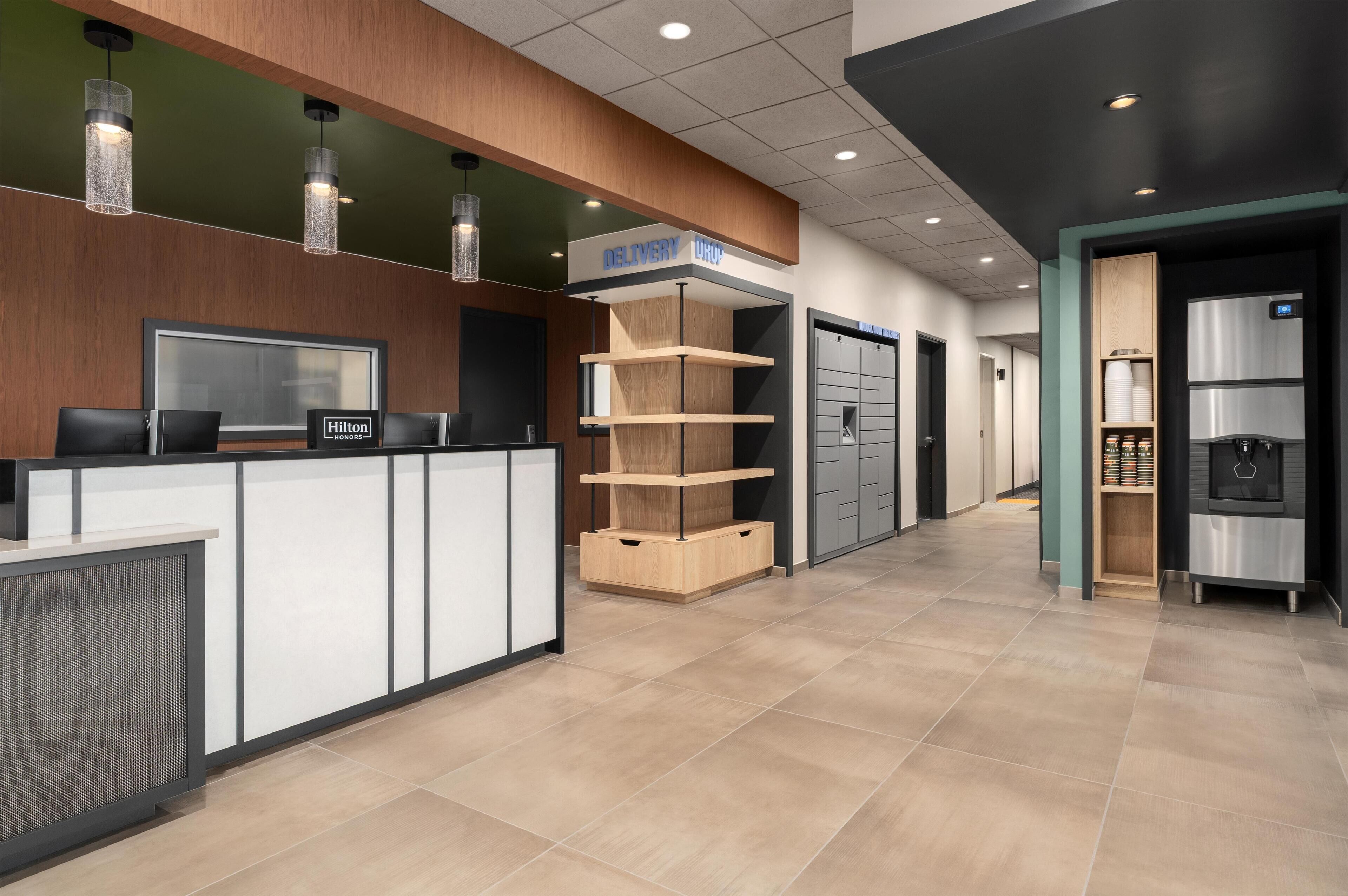 A hotel reception area with a counter, a sign for 'DELIVERY', and a refrigerator.