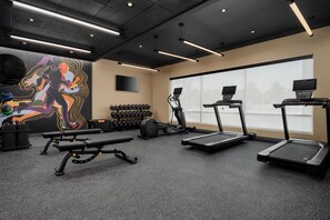 Une salle de sport équipée de tapis de course, de bancs de musculation, d’haltères et d’une grande fresque murale destinée à motiver les utilisateurs.
