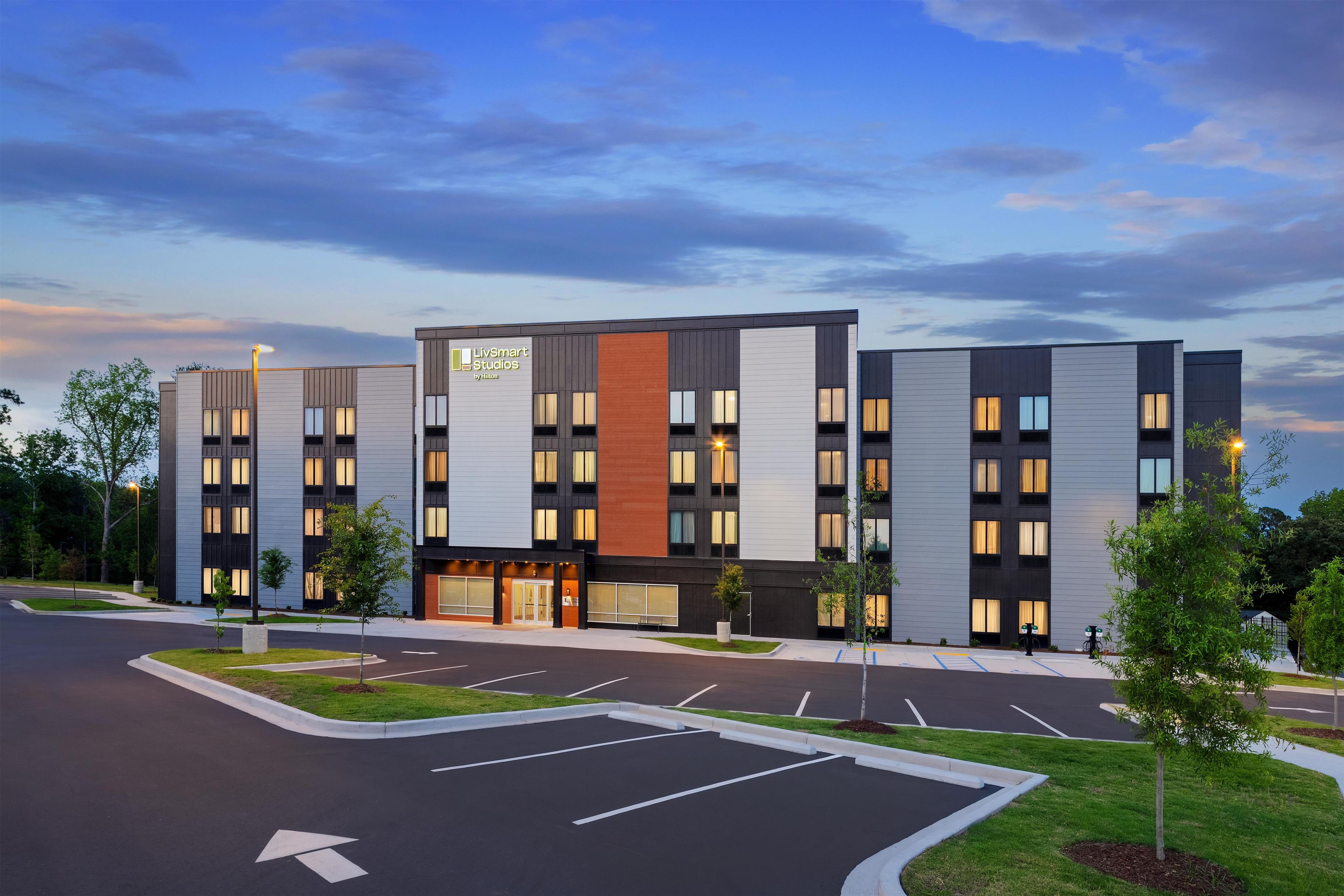 A modern hotel building with a flat roof, multiple windows, and a parking lot.