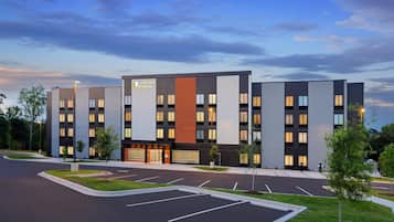 A modern hotel building with a flat roof, multiple windows, and a parking lot.