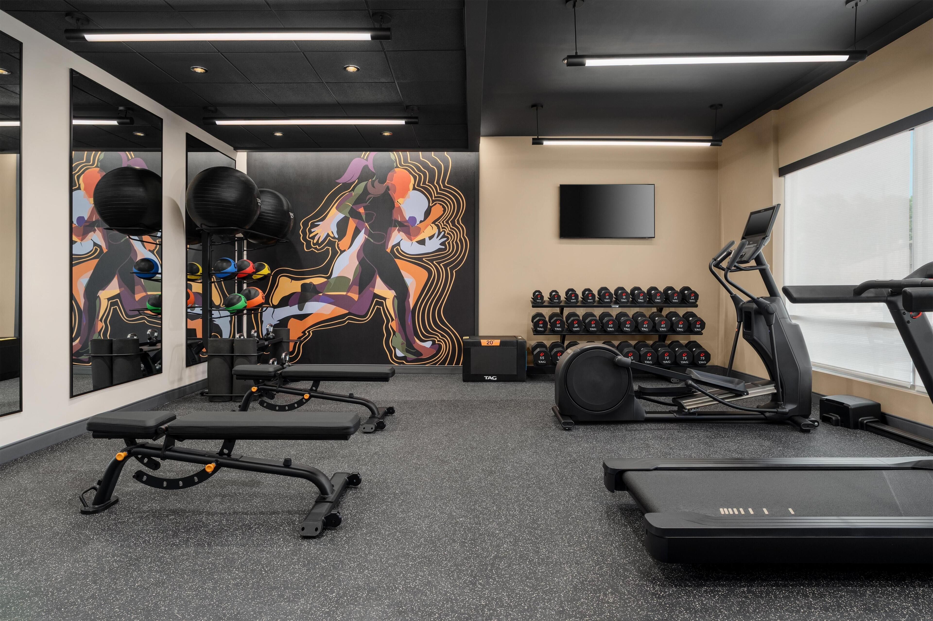 Un gimnasio con equipamiento de ejercicio, una cinta de correr y una pared con un mural colorido.