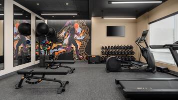 Un gimnasio con equipamiento de ejercicio, una cinta de correr y una pared con un mural colorido.
