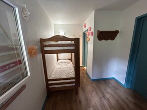 Un couloir étroit avec un lit superposé, une fenêtre donnant sur un paysage agréable et une porte dotée d’un cadre bleu.