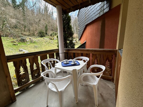 Un balcon avec une table et des chaises, une vue sur une zone boisée et un bâtiment avec un mur rouge.