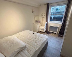Ein Schlafzimmer mit Bett, Schreibtisch, Stuhl, Heizkörper und einem Fenster mit Blick auf Gebäude.