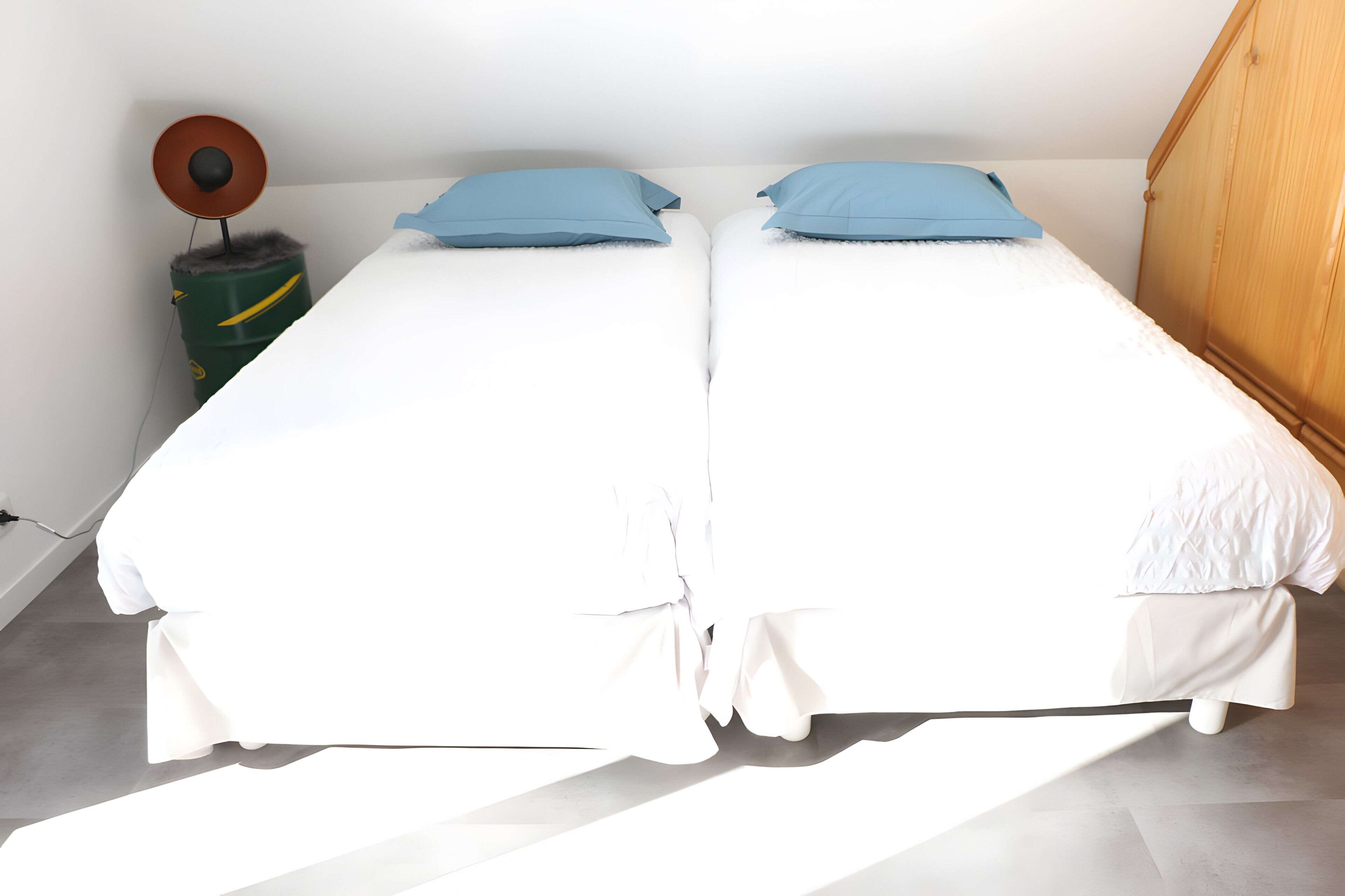 Habitación doble con dos camas, un armario de madera y una mesita con lámpara.
