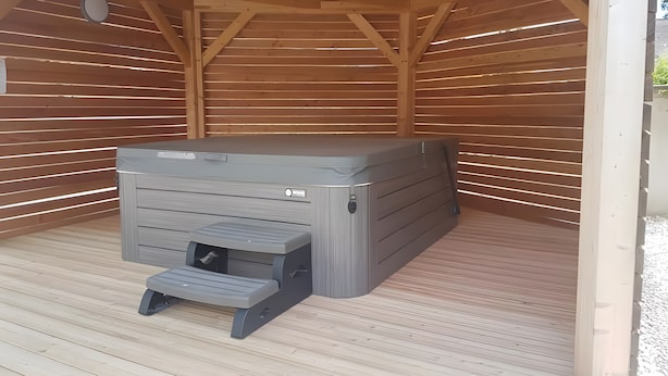 Una sauna con un banco, un panel de control, vigas de madera y suelo de madera.