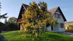 Una casa de dos pisos con un balcón, un césped cuidado y un árbol en la fachada.