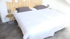 Una cama bien hecha con ropa de cama blanca y dos almohadas, un cabecero de madera, una mesita de noche con una lámpara y un enchufe.
