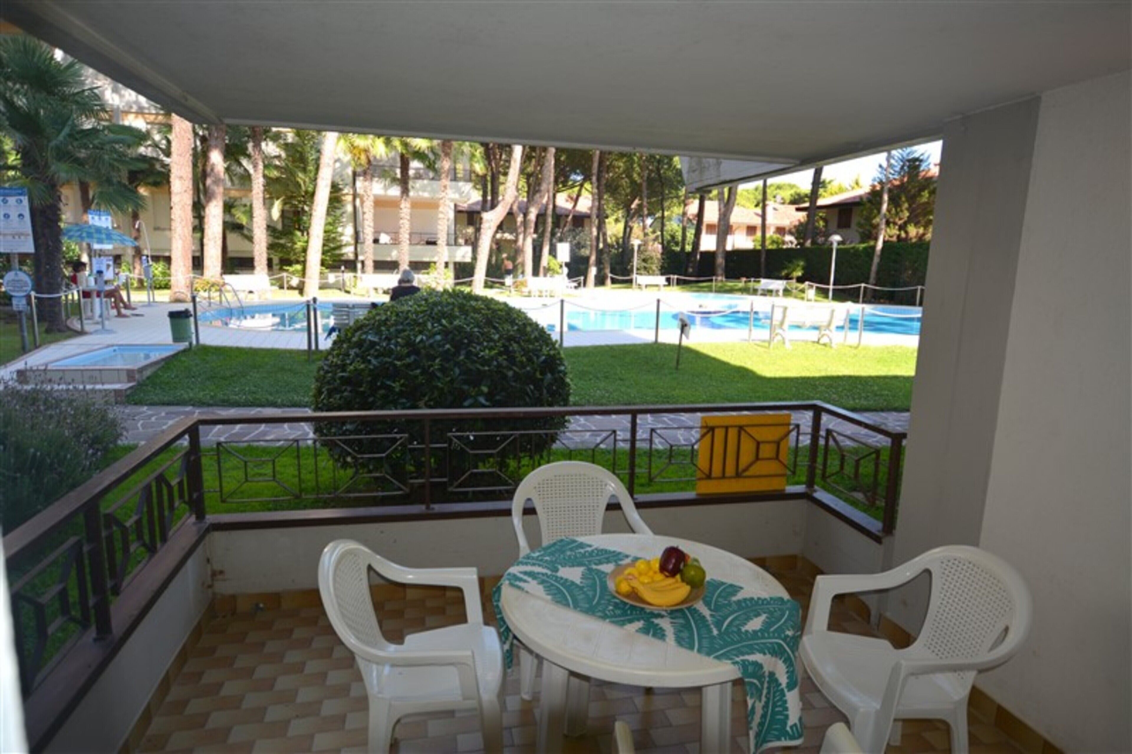 A balcony with a table and chairs, overlooking a swimming pool and a grassy area with palm trees.