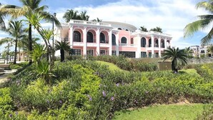 A large, multi-story building with arched windows and a pink facade, surrounded by lush greenery and palm trees. - Canisa Villas (Phu Quoc)