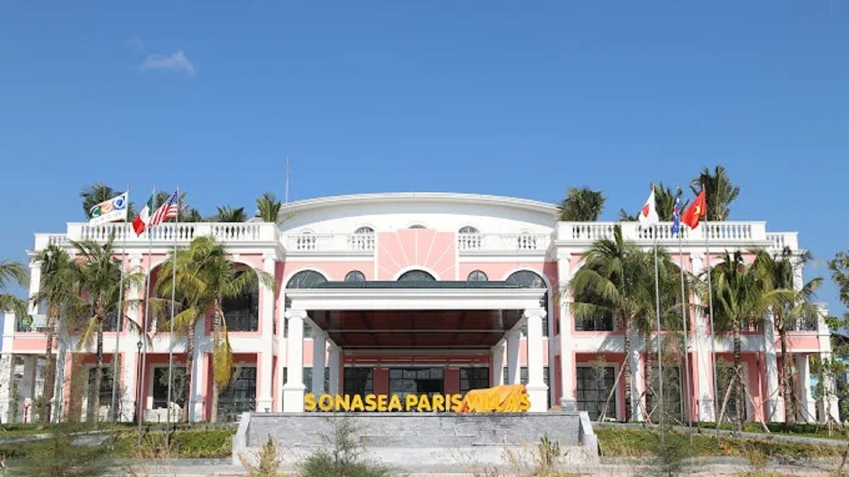 A building with a central entrance, palm trees, and multiple flags.