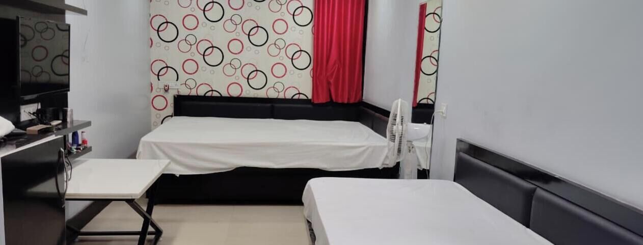A hotel room with a bed, a desk, a chair, and a standing fan.