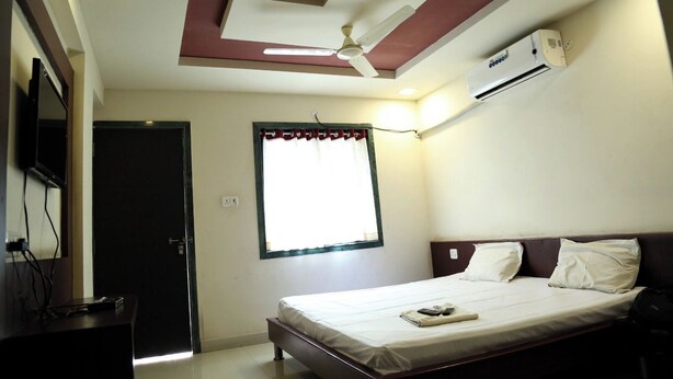 Un dormitorio con cama, ventilador de techo, equipo de aire acondicionado, ventana con cortinas y televisor sobre un mueble.