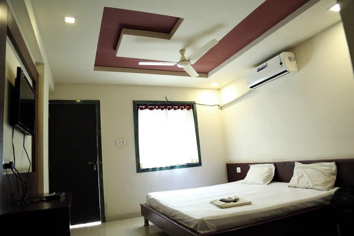 A bedroom with a bed, a ceiling fan, an air conditioning unit, a window with curtains, and a television on a stand.