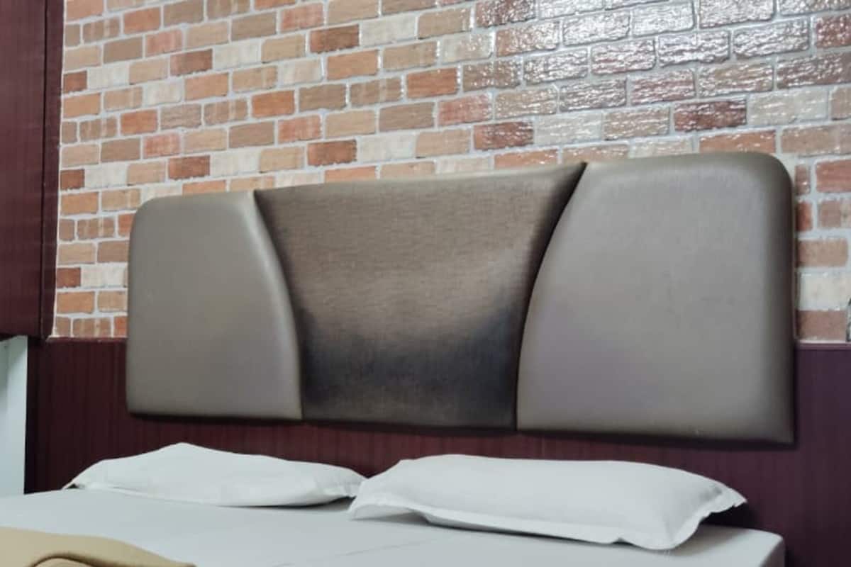A hotel room with a brick wall, a wooden wardrobe, a bed with white bedding, and a headboard.