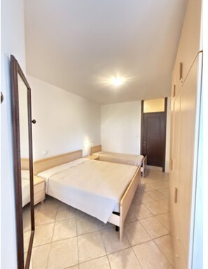 A bedroom with a large bed, a bedside table, a wardrobe, and a door. - Beachside and equipped apartment (Lignano Sabbiadoro)